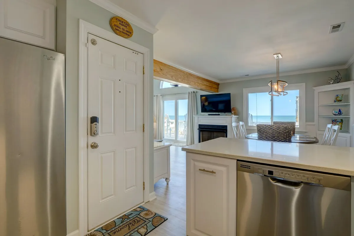 An inviting kitchen and dining area with a kitchen island, featuring large windows that offer sweeping ocean views. The scene is relaxed, with natural light pouring in, highlighting the seamless blend between indoor comfort and the stunning coastal setting.