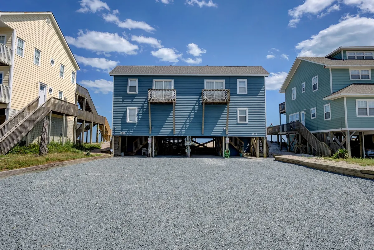 A cheerful, inviting exterior shot displaying vibrantly painted blue, yellow, and green houses with a gravel driveway. The scene suggests a relaxed, family-friendly neighborhood where outdoor activities like barbecues, games, and gatherings take place. Balconies and porches offer spaces for enjoying sunsets or morning coffee, capturing the spirit of vacation fun and togetherness.