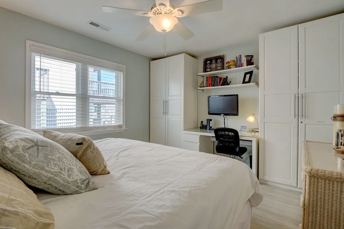 A tranquil bedroom featuring a comfortable bed with decorative pillows, a desk with a computer setup, and a large closet. The room is bathed in natural light, creating a cozy and productive atmosphere ideal for both relaxation and remote work.