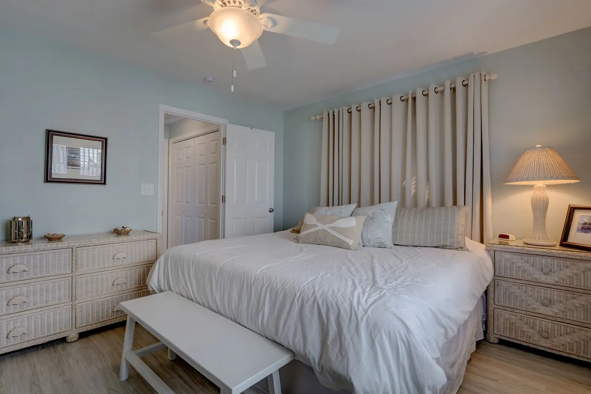 A serene bedroom with a neatly made bed, elegant dressing table, soft curtains, and a warm lamp. The room exudes calm and comfort, ideal for unwinding after a day by the coast.
